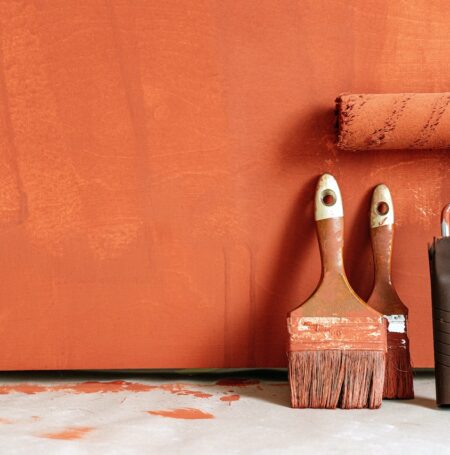 Zdjęcie przedstawiające wałek oraz dwa pędzle prze brązową ścianą